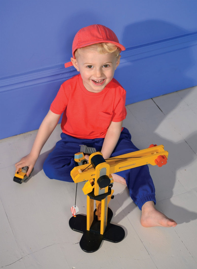 Child playing with yellow wooden crane construction toy on floor
