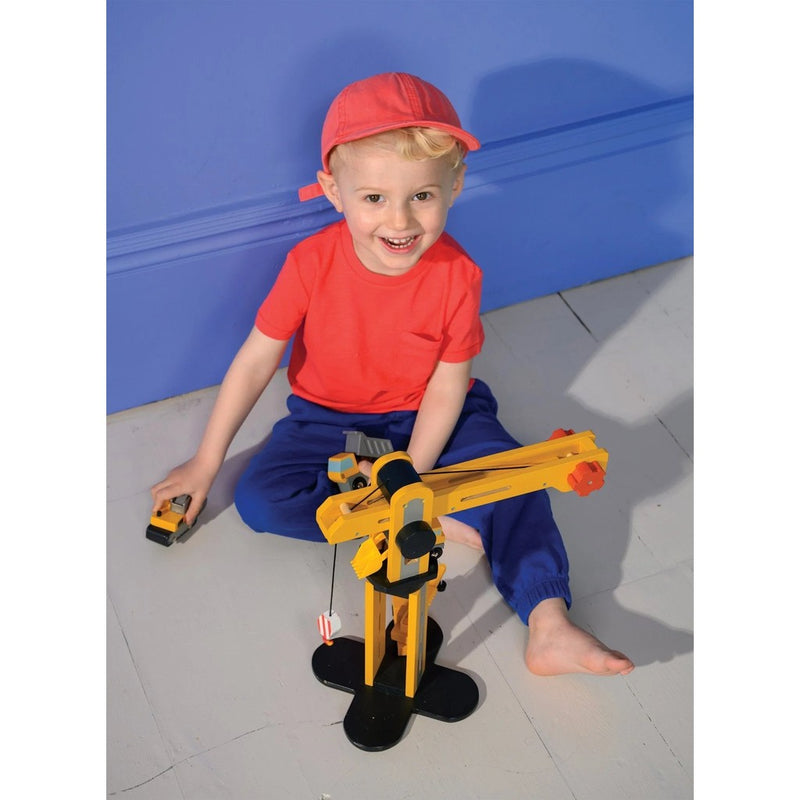 Child playing with yellow wooden crane construction toy on floor