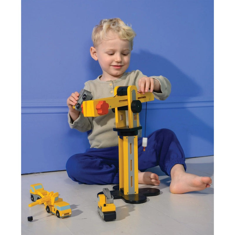 Child playing with yellow wooden crane toy and construction vehicles on blue background