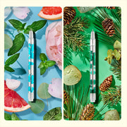 Two scented lava pens with blue and green liquid chambers displayed with natural botanical elements
