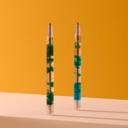Two clear pens with blue and green liquid elements on orange background
