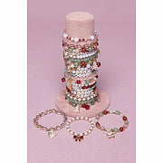 Holiday themed charm bracelets displayed on cylindrical stand with pink background