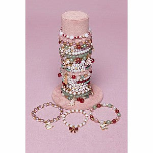 Holiday themed charm bracelets displayed on cylindrical stand with pink background