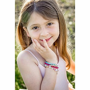 Young girl wearing colorful beaded holiday bracelet, smiling with hand near face