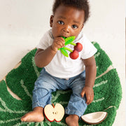 Baby playing with Mery the Cherry teething toy on green blanket