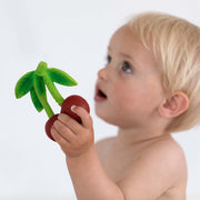 Baby holding Mery the Cherry teething toy with green palm leaves