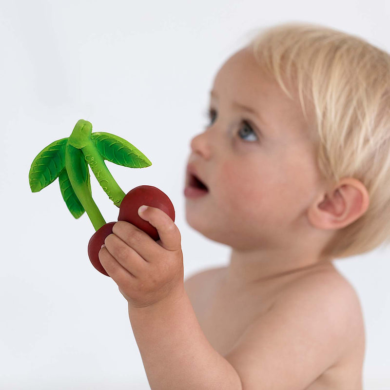 Baby holding Mery the Cherry teething toy with green palm leaves