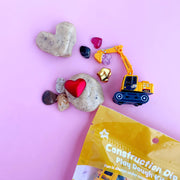 Valentine's construction play dough kit with toy excavator, heart shapes, and gemstones on pink background
