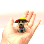 Small cartoon dog figurine with hat and blue shirt held in open palm