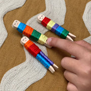 Finger touching completed, colorful wooden worry dolls with embroidery thread on knitted fabric background.