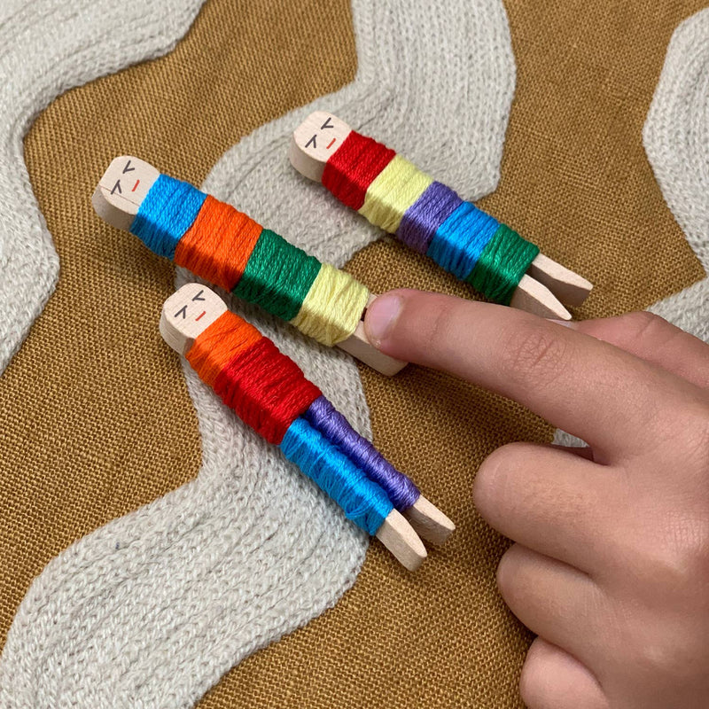 Finger touching completed, colorful wooden worry dolls with embroidery thread on knitted fabric background.