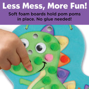 Child's hand placing pom poms on foam dinosaur craft board with googly eyes