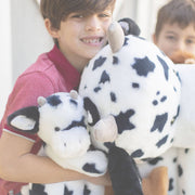 Child hugging large white and black spotted cow plushie stuffed animal