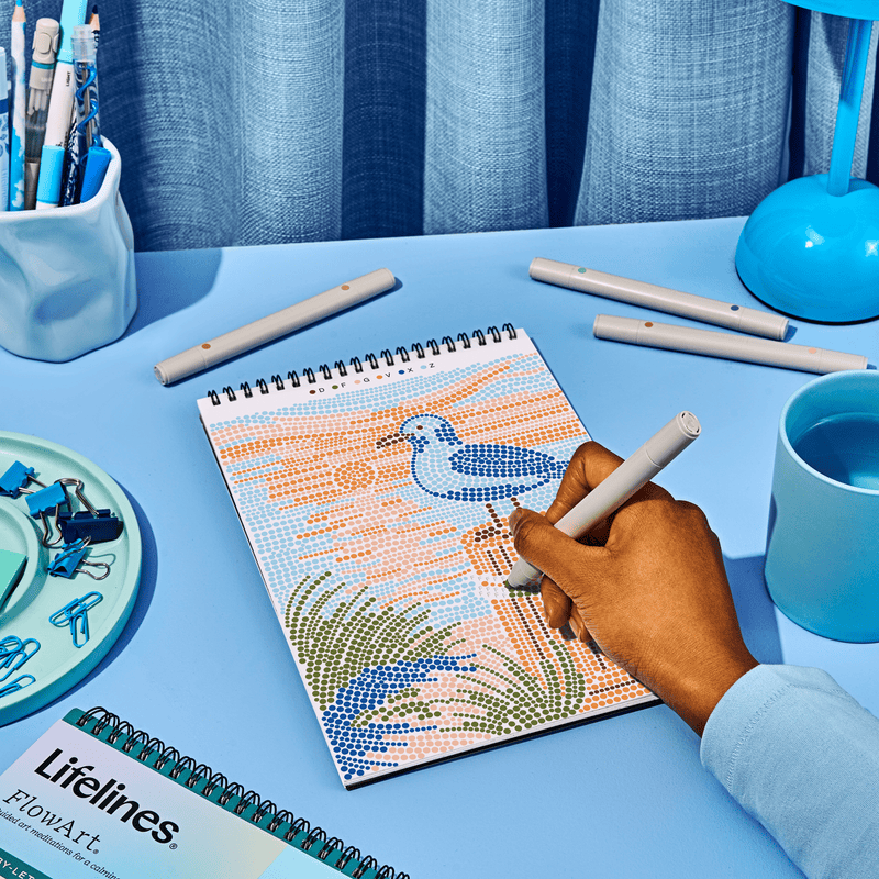 Person using FlowArt dot-by-letter drawing pad showing beach scene with seagull pattern