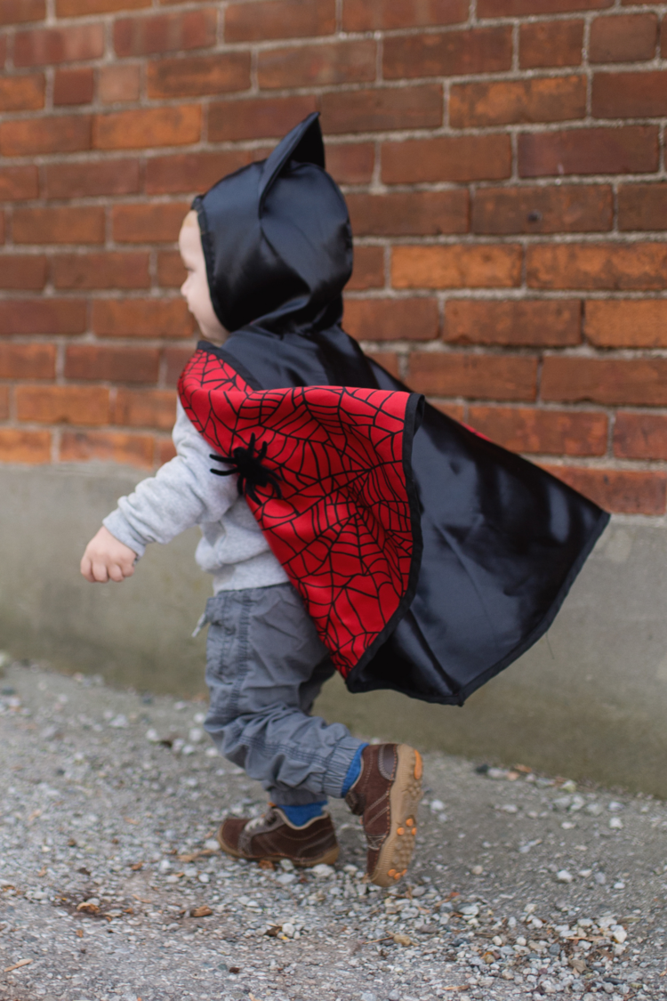 Child wearing reversible spider and bat cape running outdoors