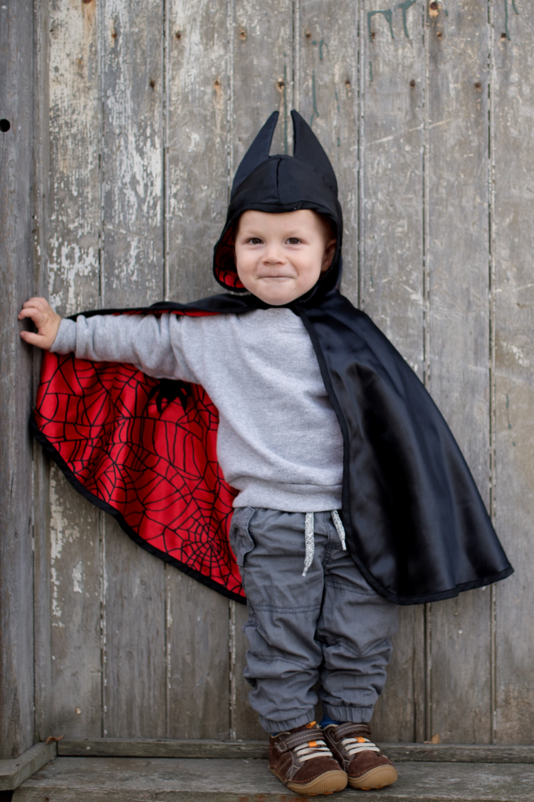 Child wearing reversible superhero cape with black exterior and red interior with web pattern