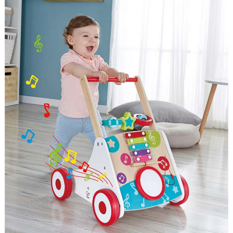 Smiling toddler pushing Hape musical activity walker with xylophone and drum on wood floor