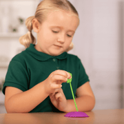 Child using purple butterfly feeder with green feeding tube in classroom setting
