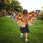 Child wearing orange Painted Lady butterfly wings running in grassy outdoor setting