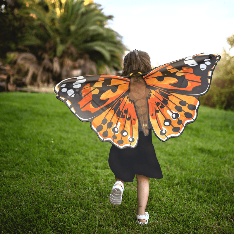 Child wearing orange Painted Lady butterfly wings running in grassy outdoor setting