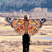 Child wearing orange Painted Lady butterfly wings in outdoor field setting