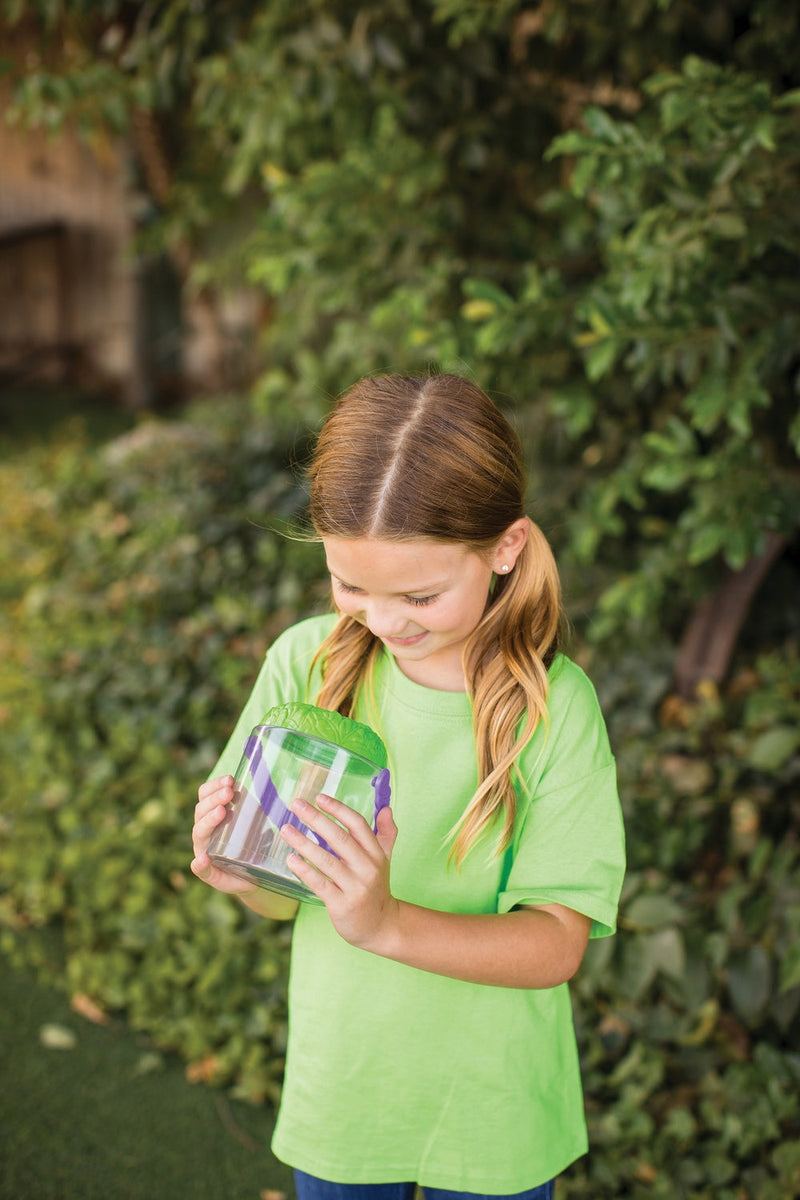 Young girl in green shirt examining insects in clear bug observation jar outdoors