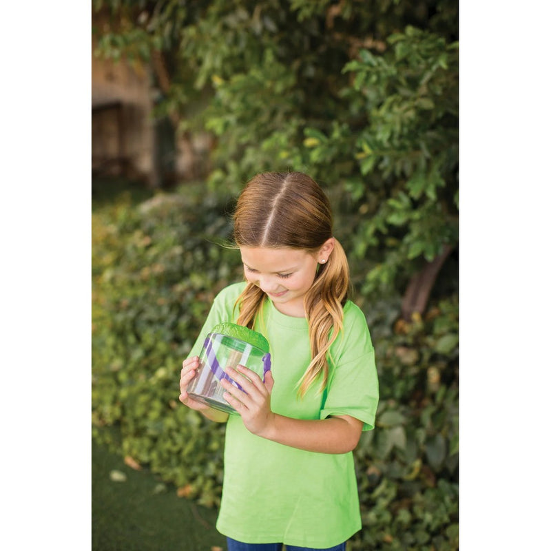 Young girl in green shirt examining insects in clear bug observation jar outdoors