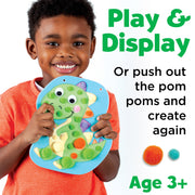 Child holding dinosaur-shaped pom pom craft toy with colorful pom poms
