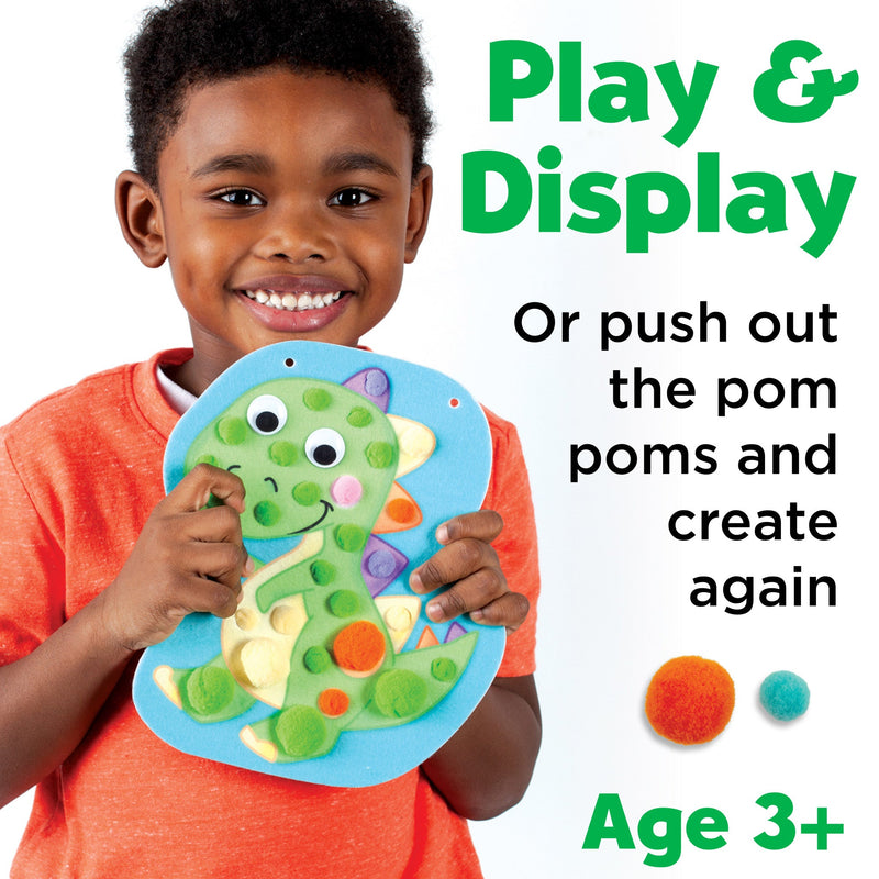 Child holding dinosaur-shaped pom pom craft toy with colorful pom poms