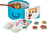 Acorn Soup children's cooking playset with blue pot, wooden spoon, recipe cards, and ingredient tokens.