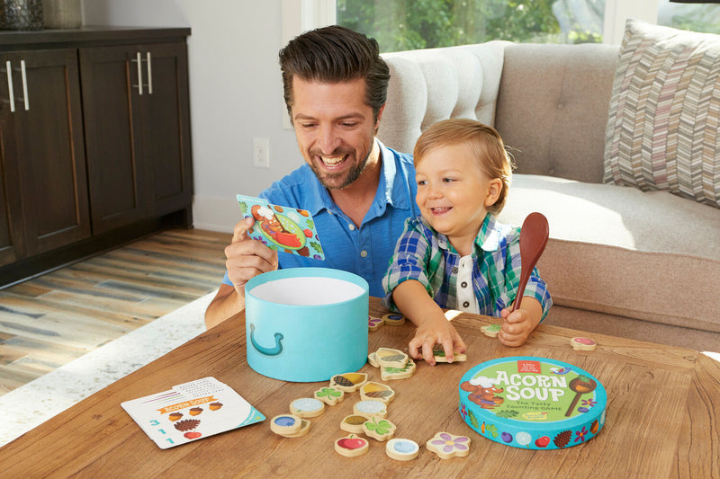 Father and child playing with Acorn Soup counting game at wooden table.