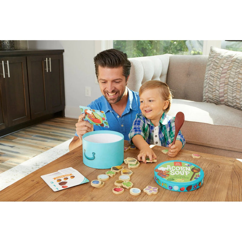 Father and child playing with Acorn Soup counting game at wooden table.
