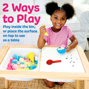Child playing with colorful sensory materials at wooden activity table with compartments