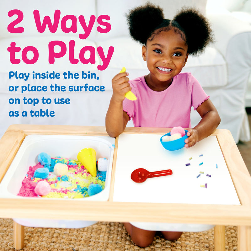 Child playing with colorful sensory materials at wooden activity table with compartments