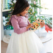 Child in pink dress holding orange robot toy near Christmas tree