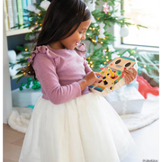 Child in pink dress holding orange robot toy near Christmas tree