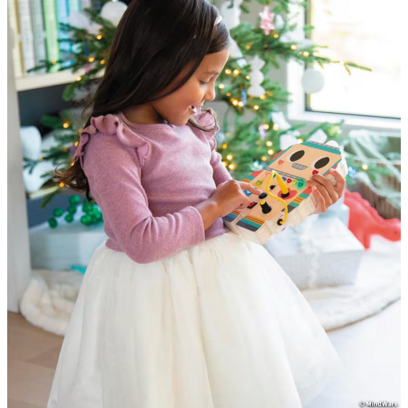 Child in pink dress holding orange robot toy near Christmas tree