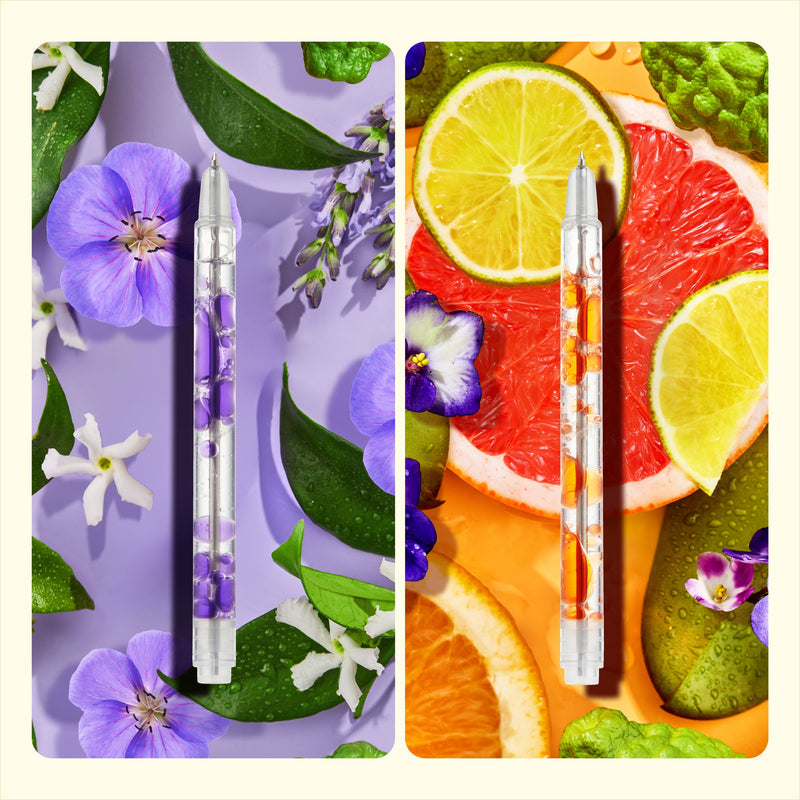 Two scented lava pens with purple and orange liquid surrounded by flowers and citrus fruits