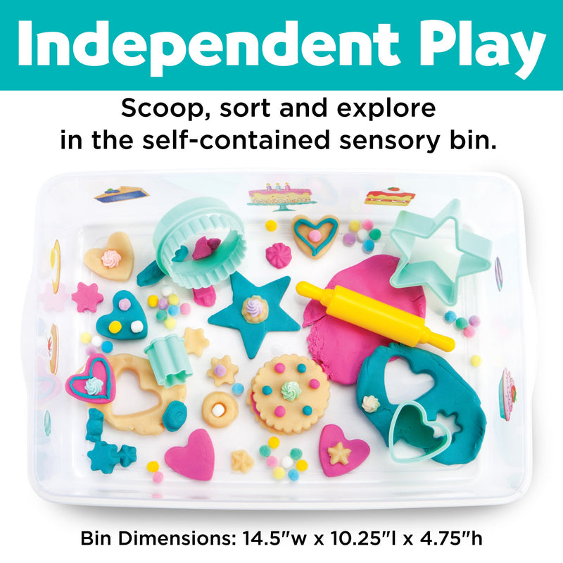 Colorful sensory bin with baking-themed play items including cookie cutters, stars, hearts, and rolling pin
