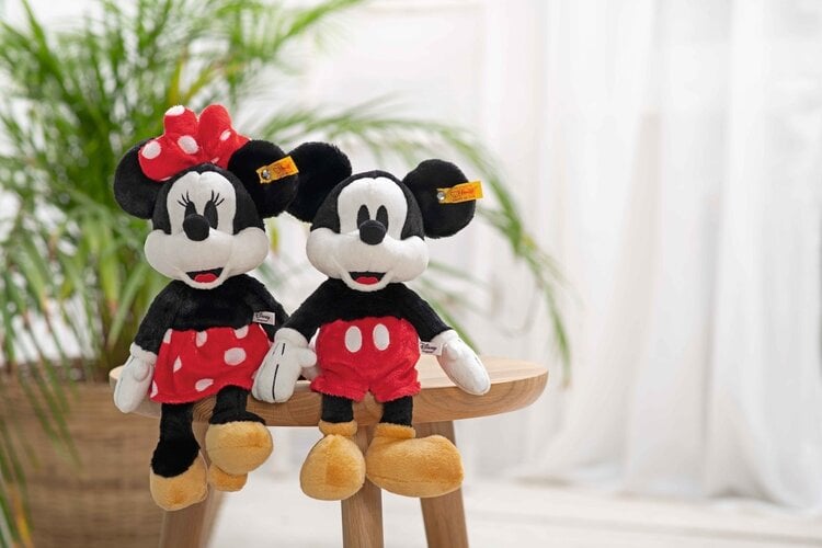 Mickey and Minnie Mouse plush toys sitting together on wooden furniture