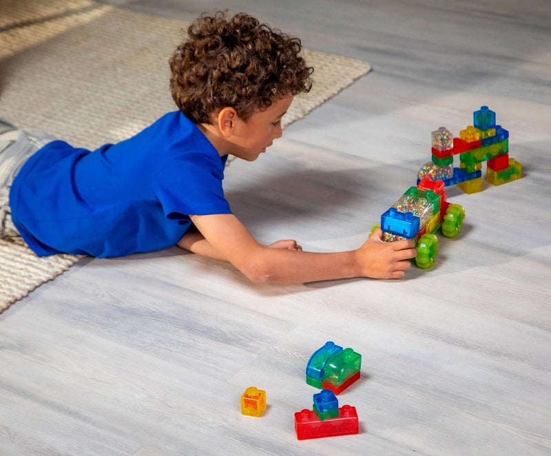 Child playing with colorful translucent building blocks on wooden floor creating truck