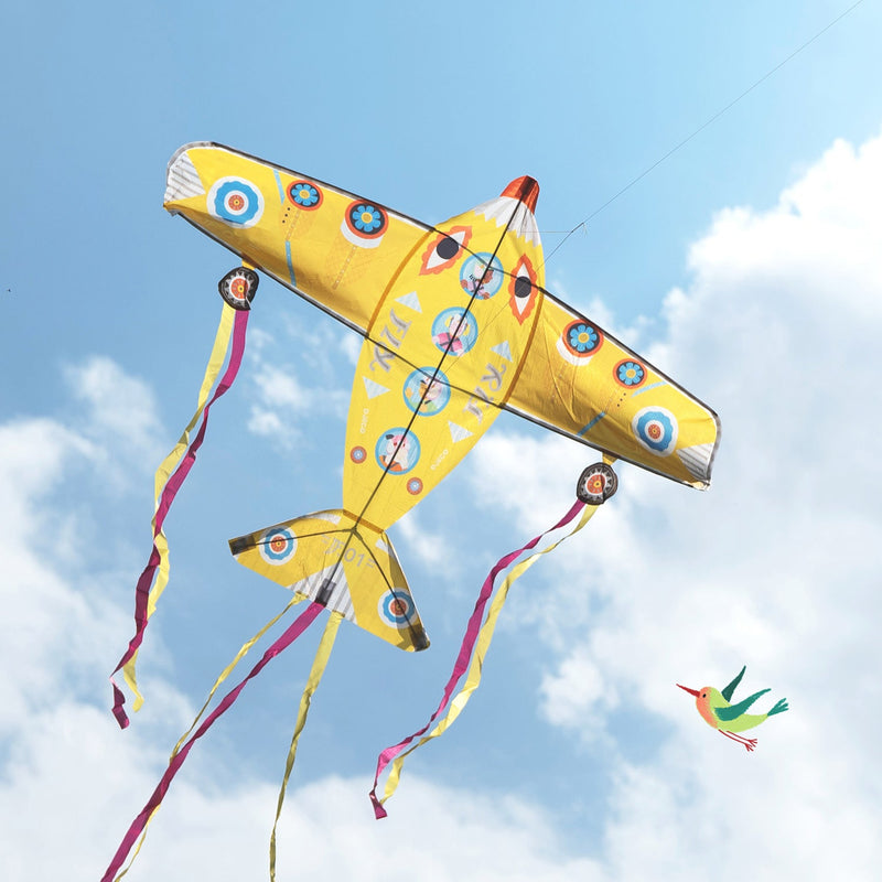 Yellow airplane kite with colorful circular patterns flying against blue sky with clouds