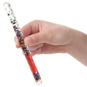 Hand holding clear tube wand filled with colorful glitter and red liquid