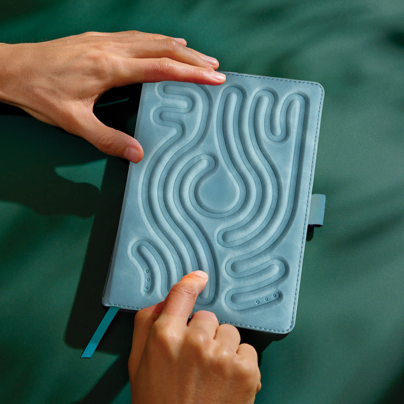 Hands touching blue tactile notebook with raised contour patterns on cover