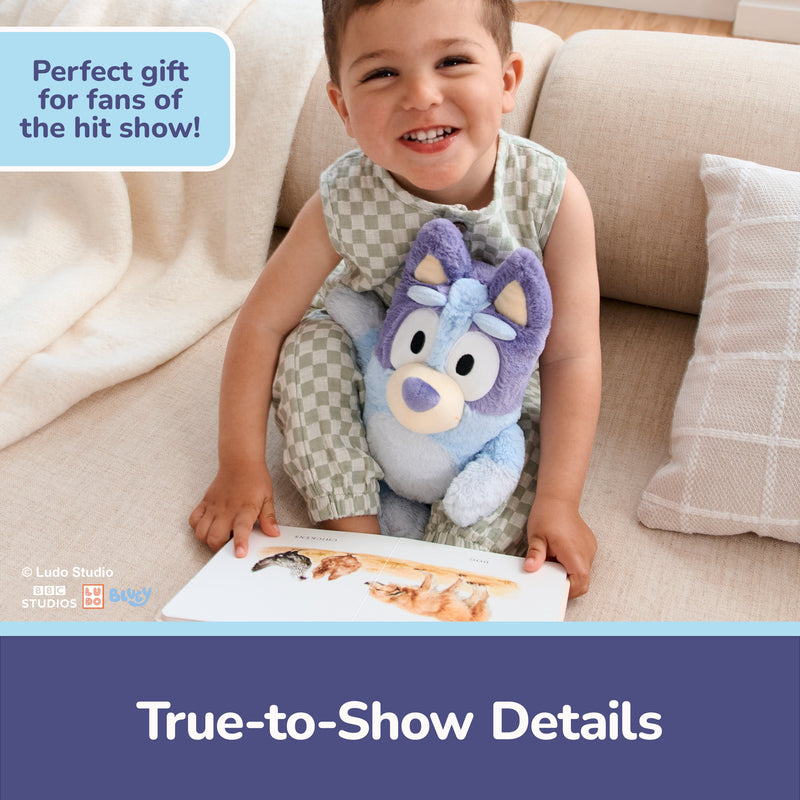 Child holding blue Bluey plush toy while reading book on couch